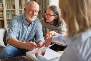 Mature couple sitting down with attorney to discuss and sign legal documents
