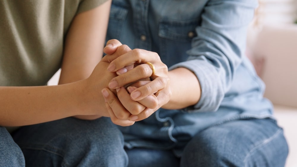 Two people clasping hands and supporting each other while grieving