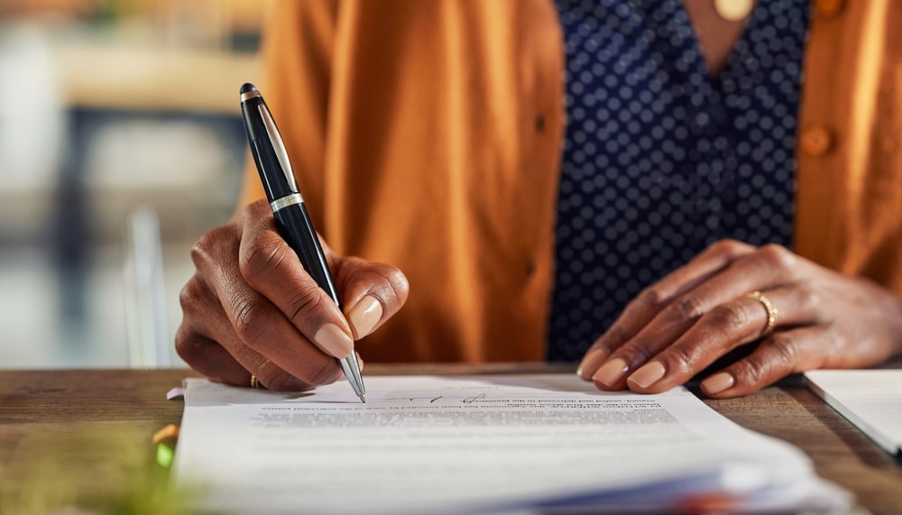 Woman in mustard yellow cardigan sitting at table, signing documents