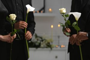 Three people standing together, wearing black and holding white lilies
