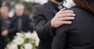 Man putting comforting hand on shoulder of a mourner at a funeral or gathering