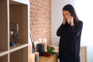Young woman wearing black, crying as she stands in front of a black cremation urn