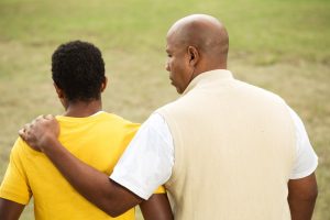 male guardian in light yellow shirt resting his hand on a teen boy's shoulder