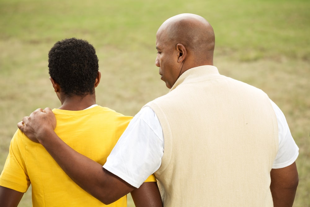 male guardian in light yellow shirt resting his hand on a teen boy's shoulder