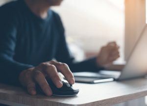 Man at home at his desk working on the computer, hand on mouse