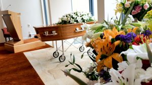 Casket with flowers resting on top placed in front of a room near a podium