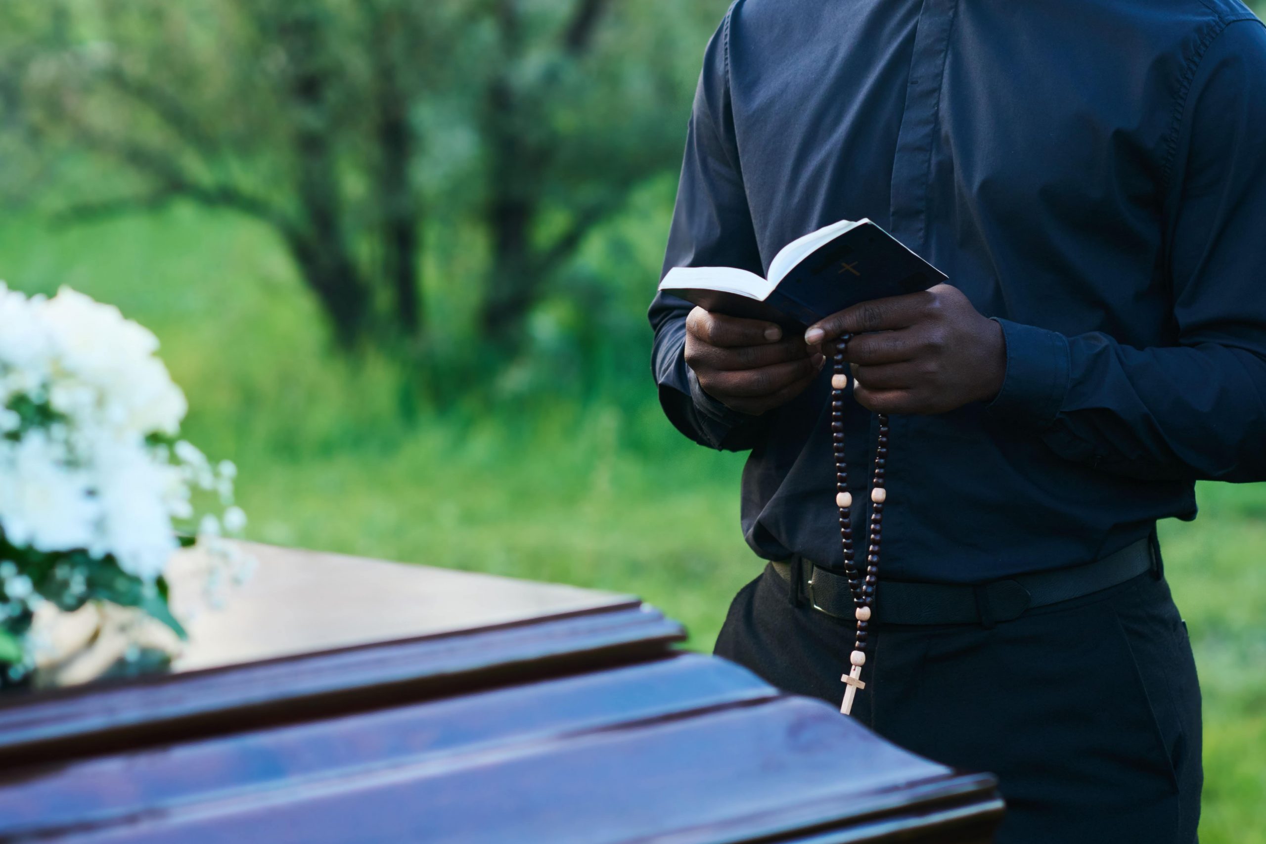 Man standing by a casket reading aloud from a book