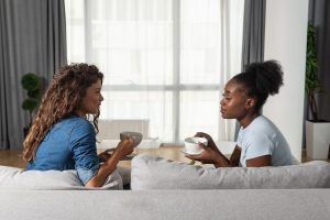 Two friends sitting on a couch drinking coffee and talking