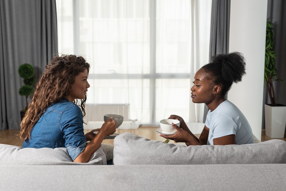 Two friends sitting on a couch drinking coffee and talking
