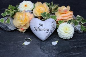 peach and white flowers on a grave with a heart-shaped stone engraved with "In Memory"