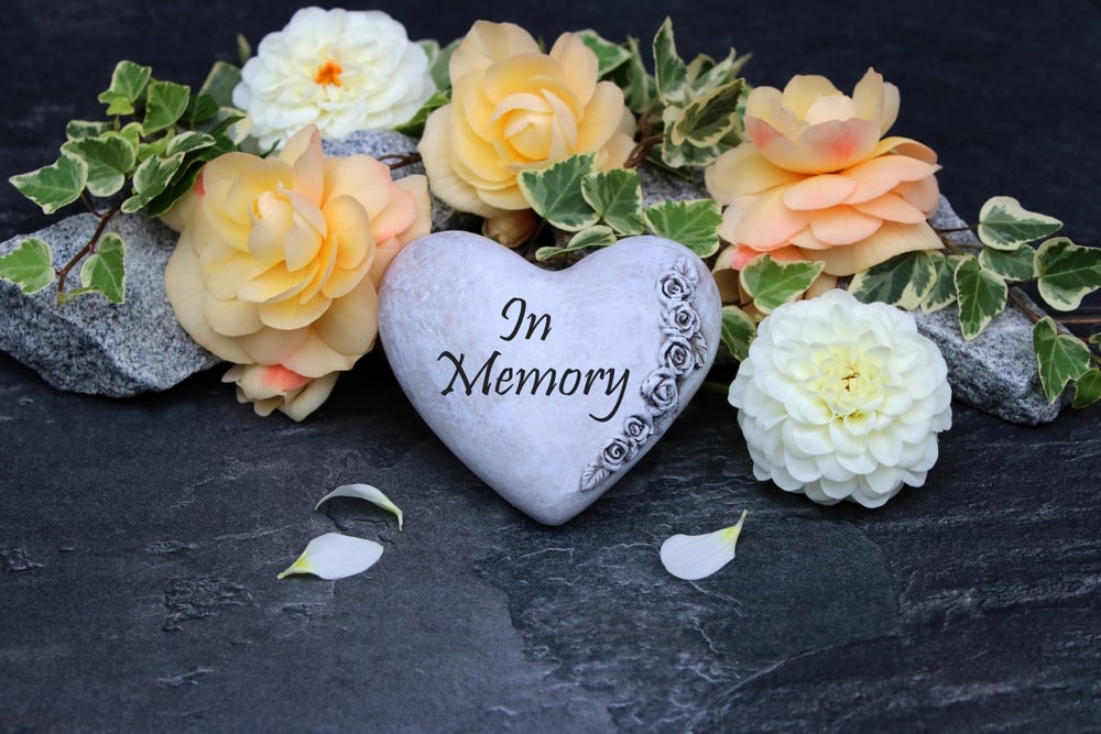 peach and white flowers on a grave with a heart-shaped stone engraved with "In Memory"