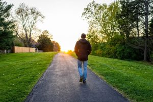 Man walking alone outside on a paved walkway with trees and green grass