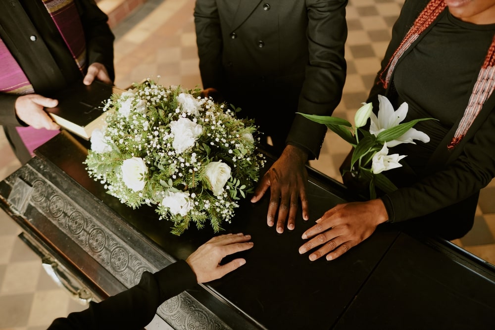 Mourners attending a service, placing hands on casket in remembrance