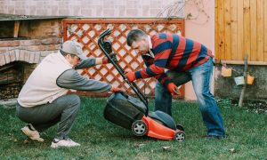 Two men working on a lawn mower; friend offering practical help