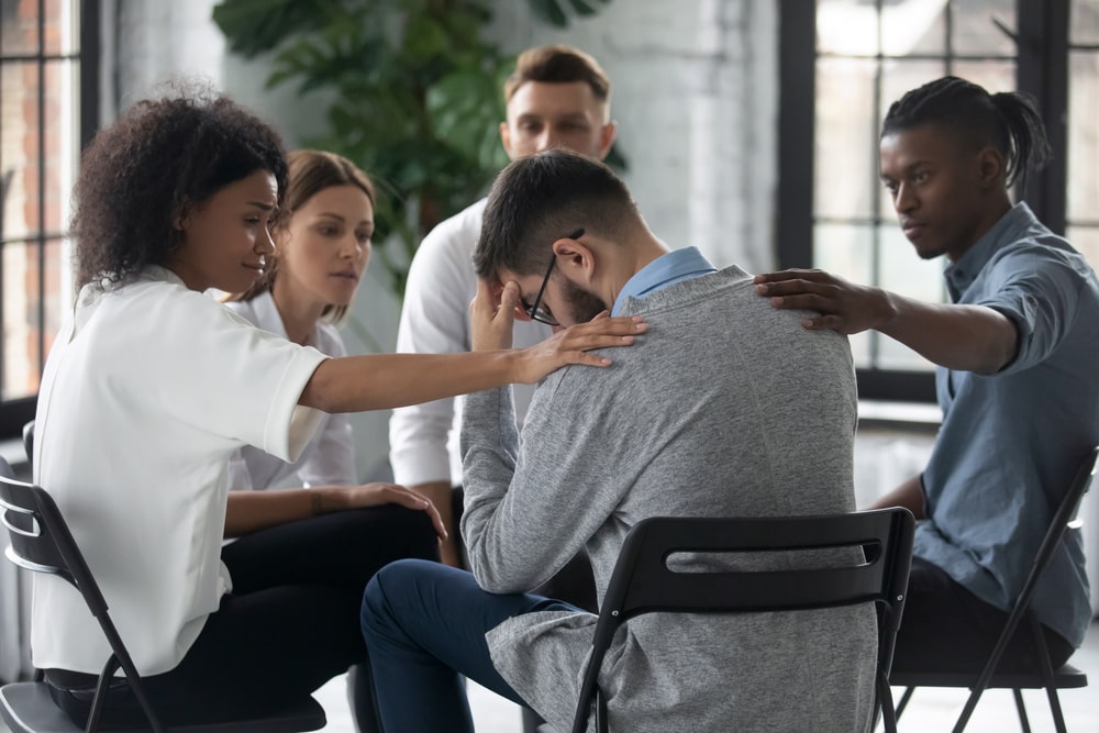 woman and man placing hands on a crying man's shoulders at a grief support group