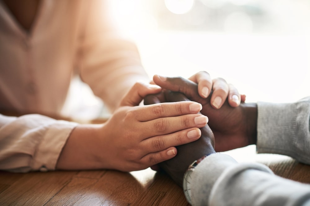 woman resting her hands on a man's clasped hands, comforting him