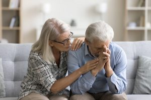 woman comforting her husband while he rests his face on his hands