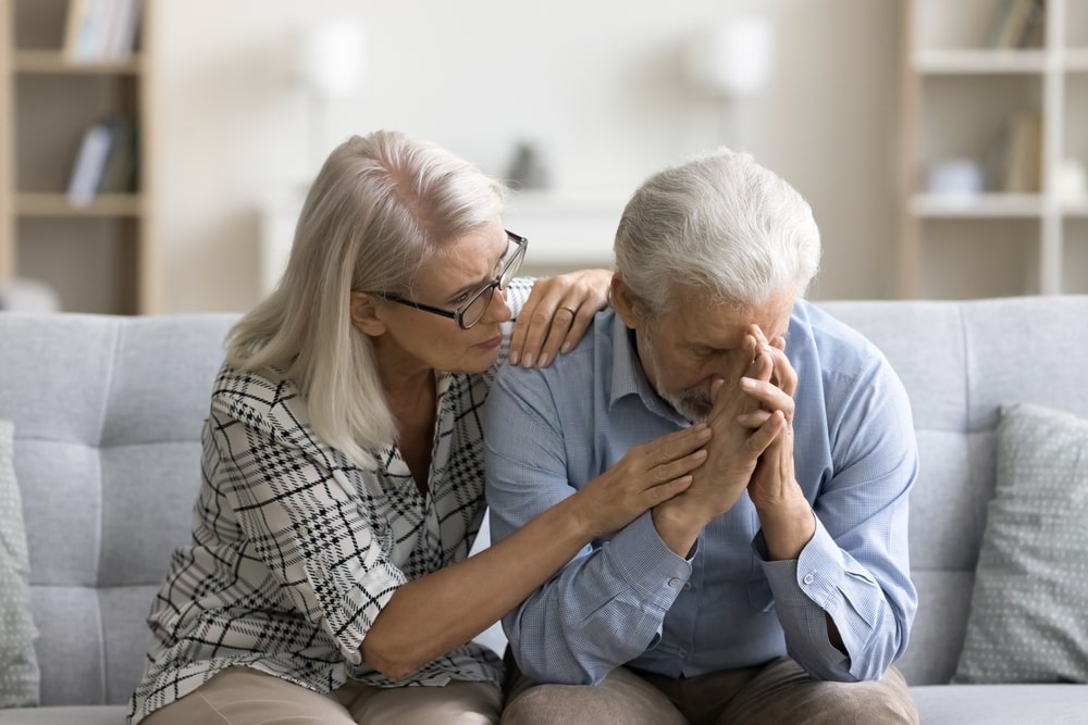 woman comforting her husband while he rests his face on his hands