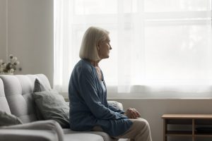 Mature woman sitting forlornly at home; looking out window; grief & depression