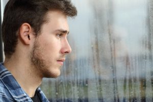 man staring out a window streaked with rain