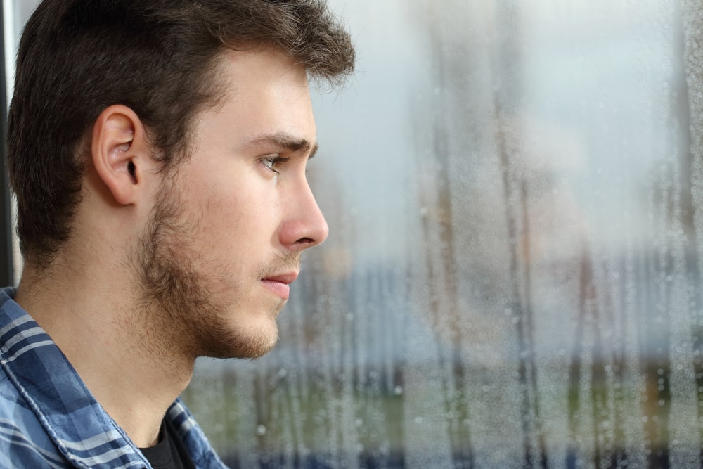 man staring out a window streaked with rain