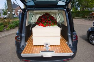 Wooden casket resting in back of hearse with red rose flower spray