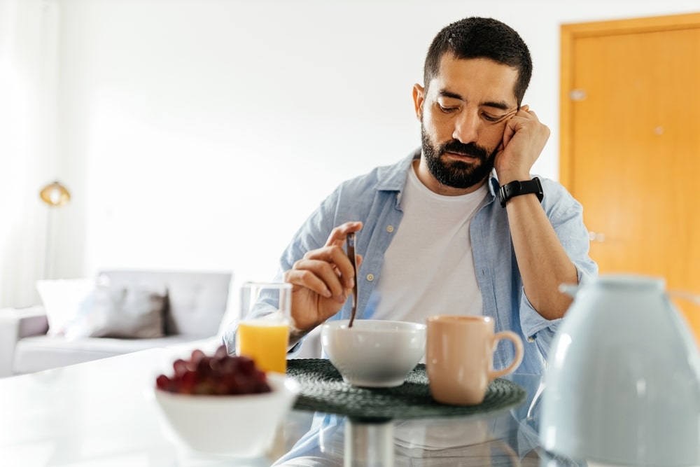 Man absently stirring food in a bowl and staring down, lost in thought