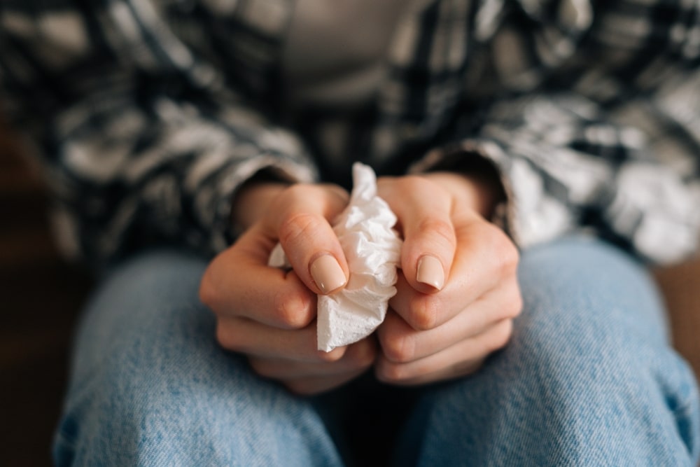 Close up of a person tightly holding onto a tissue with tense fisted hands