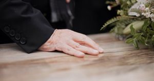 Older person resting hand on lid of wooden casket