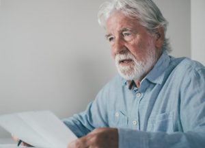 Older man in a blue shirt holding a piece of paper and rehearsing a eulogy