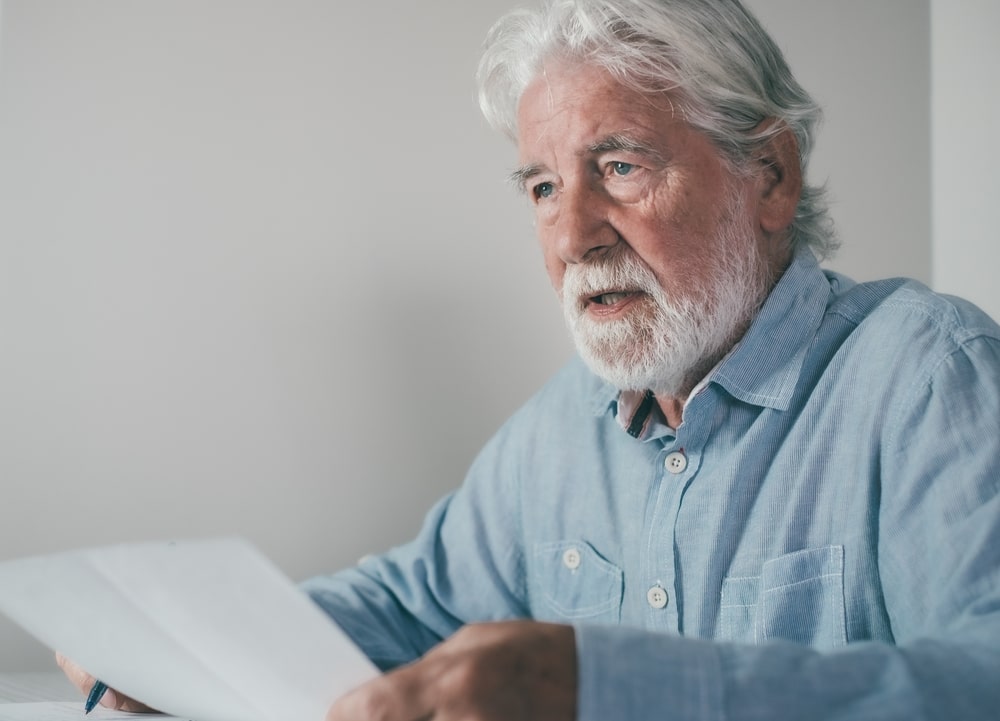 Older man in a blue shirt holding a piece of paper and rehearsing a eulogy