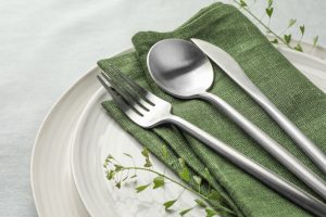 Fork, spoon, and knife resting on a green cloth napkin on top of two stacked plates