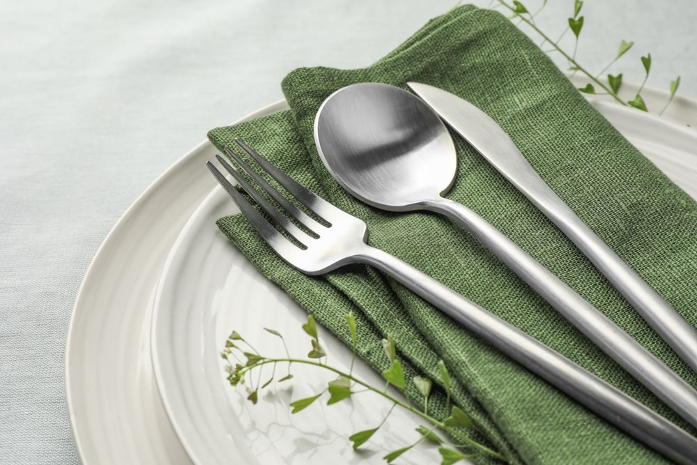 Fork, spoon, and knife resting on a green cloth napkin on top of two stacked plates