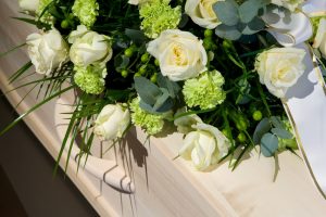 Flower spray of white roses resting on light wood casket