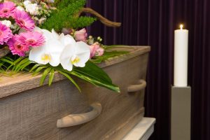 Flower spray resting on top of light wood casket with lit candle nearby