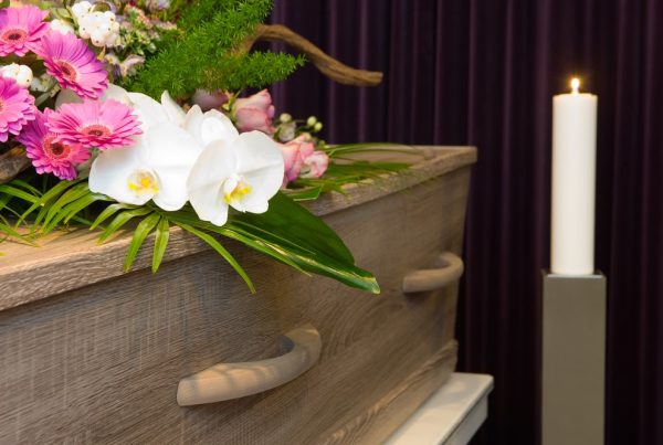 Flower spray resting on top of light wood casket with lit candle nearby