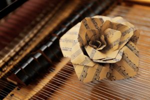Paper rose made out of music sheet resting on piano keyboard