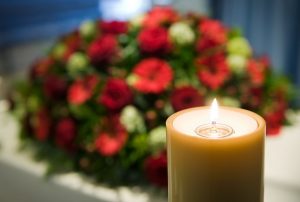Lit candle in foreground with red flower spray in background