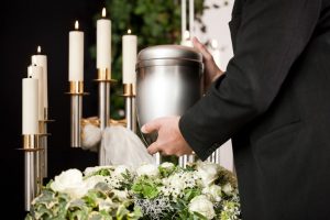 Man in black suit placing a cremation urn in a circle of white flowers for a service