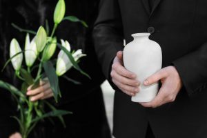 Man wearing black and holding a white urn