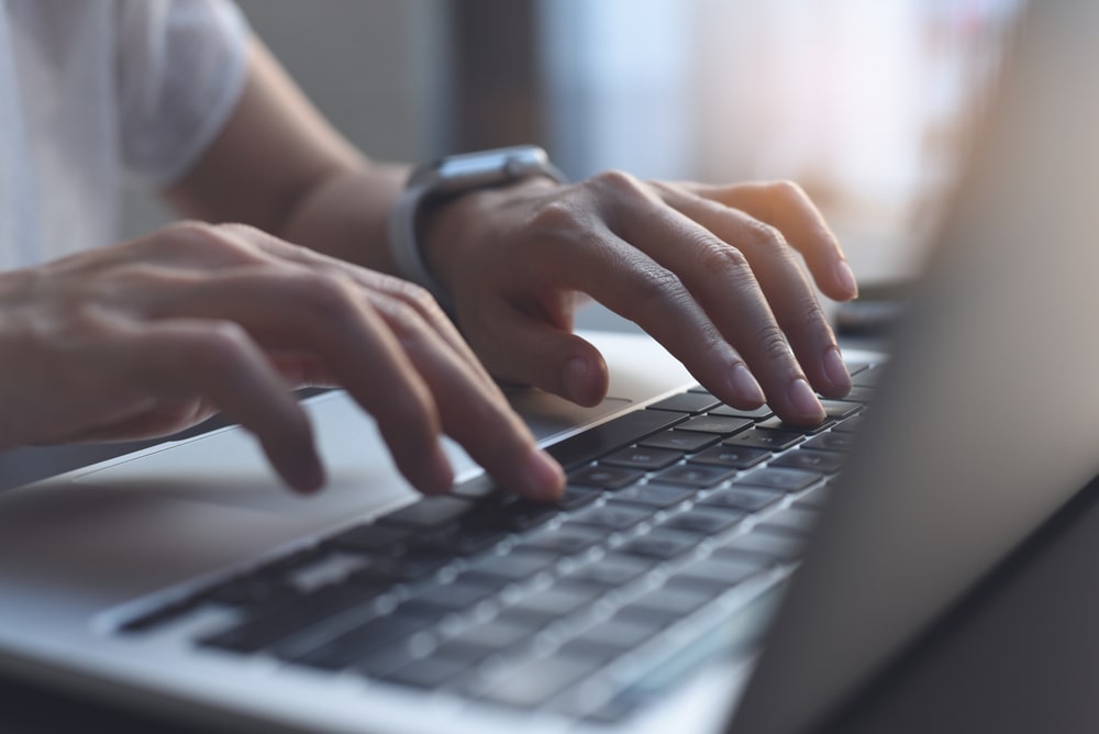 hands typing on a silver laptop with black keys