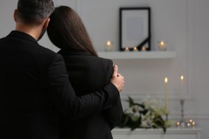 Man and woman in black clothing leaning on each other in a comforting way as they attend a visitation