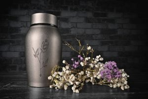 Decorative silver urn resting on a table next to white and purple flowers
