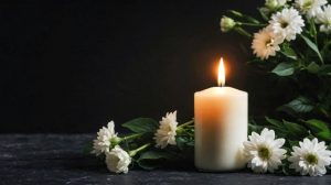 Lit memorial candle with white funeral flowers around it