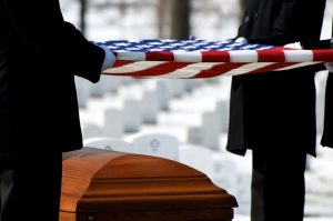 Military members in uniform folding an American flag over a casket