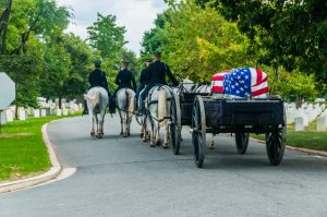 Flag-covered casket being escorted by wagon to its final resting place in a national cemetery