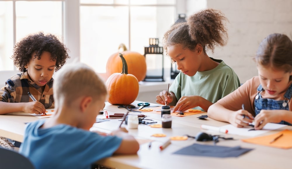Four children sitting at a table working on fall crafts