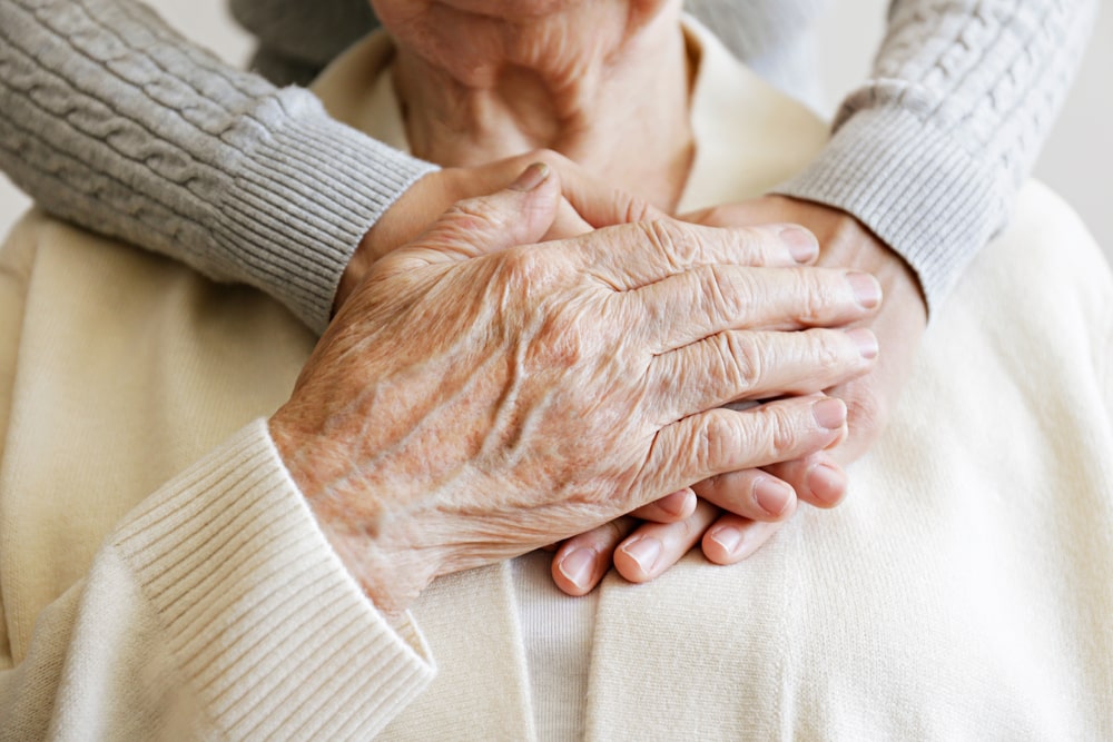 Elderly mother and adult daughter with hands on mother's heart