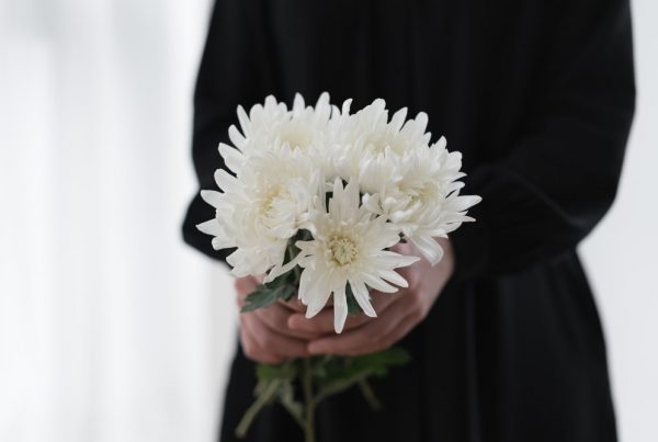 Woman wearing black clothing holding bouquet of white chrysanthemums