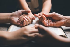 Three people sitting together holding hands and praying; focus on hands